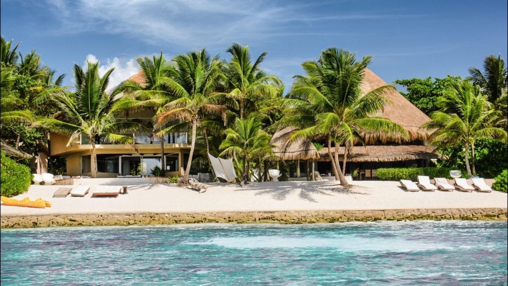 Puerto Estate villa exterior behind a sandy shore, palms and blue water — Puerto Aventuras, Mexico