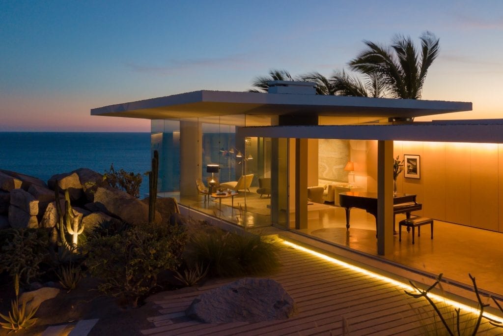 Casa Finisterra flat-roofed pavilion glowing at sunset with the piano room lit — Los Cabos, Mexico