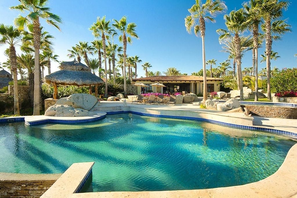 Villa Las Arenas curved pool with palapa and the villa facade beyond — Los Cabos, Mexico