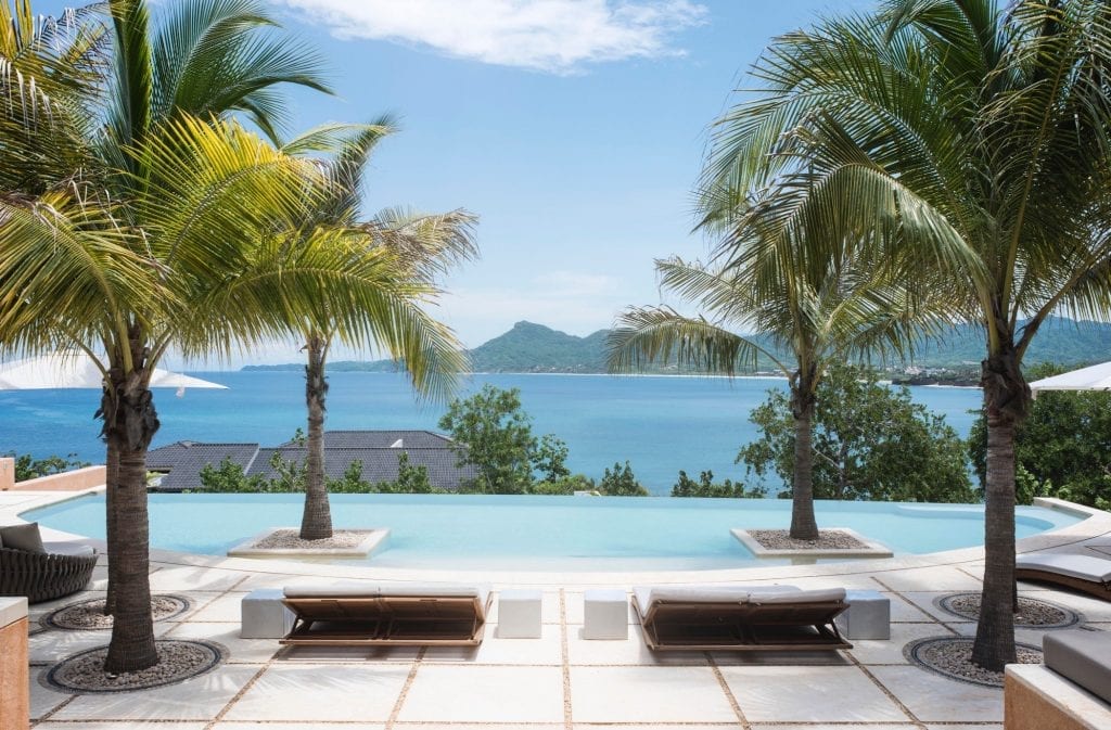 Luxury villa Kupuri 36 in Mexico with an ocean-view infinity pool, lounge chairs, and palm trees.