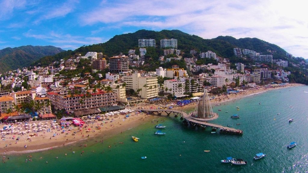 A panoramic aerial view of the Zona Romántica in Puerto Vallarta, showcasing vibrant streets, luxurious villa rentals, and the Pacific Ocean coastline.