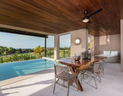 Luxury Mexican villa’s outdoor space: wooden ceiling, fan, covered dining; overlooks infinity pool and Las Marietas’ tropical landscape.