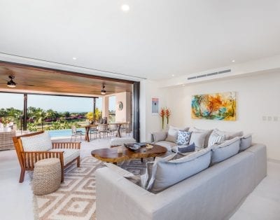 Luxury vacation villa in Mexico: Modern living room with pool view, beige sectional, wooden coffee table, vibrant artwork.