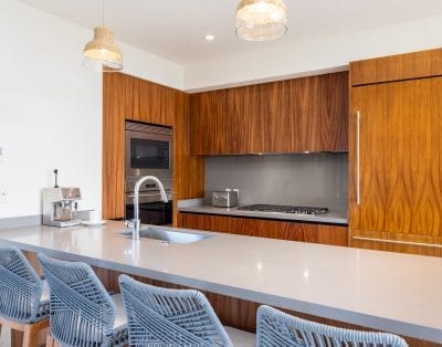 A modern kitchen in Las Marietas, Mexico, with wooden cabinets, stainless steel appliances, and gray island seating.