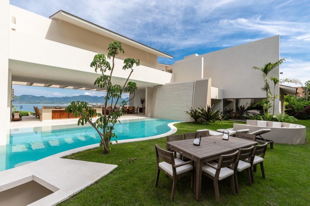 Luxurious Villa Kupuri in Mexico: sleek pool, poolside lounge with seating, dining table, lush greenery, mountain views.