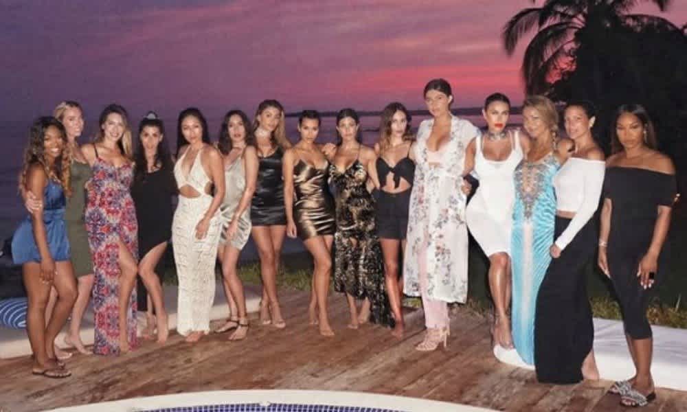 15 women in stylish outfits pose by a pool at sunset, palm trees in the background. Location: luxury villa rental in Mexico.