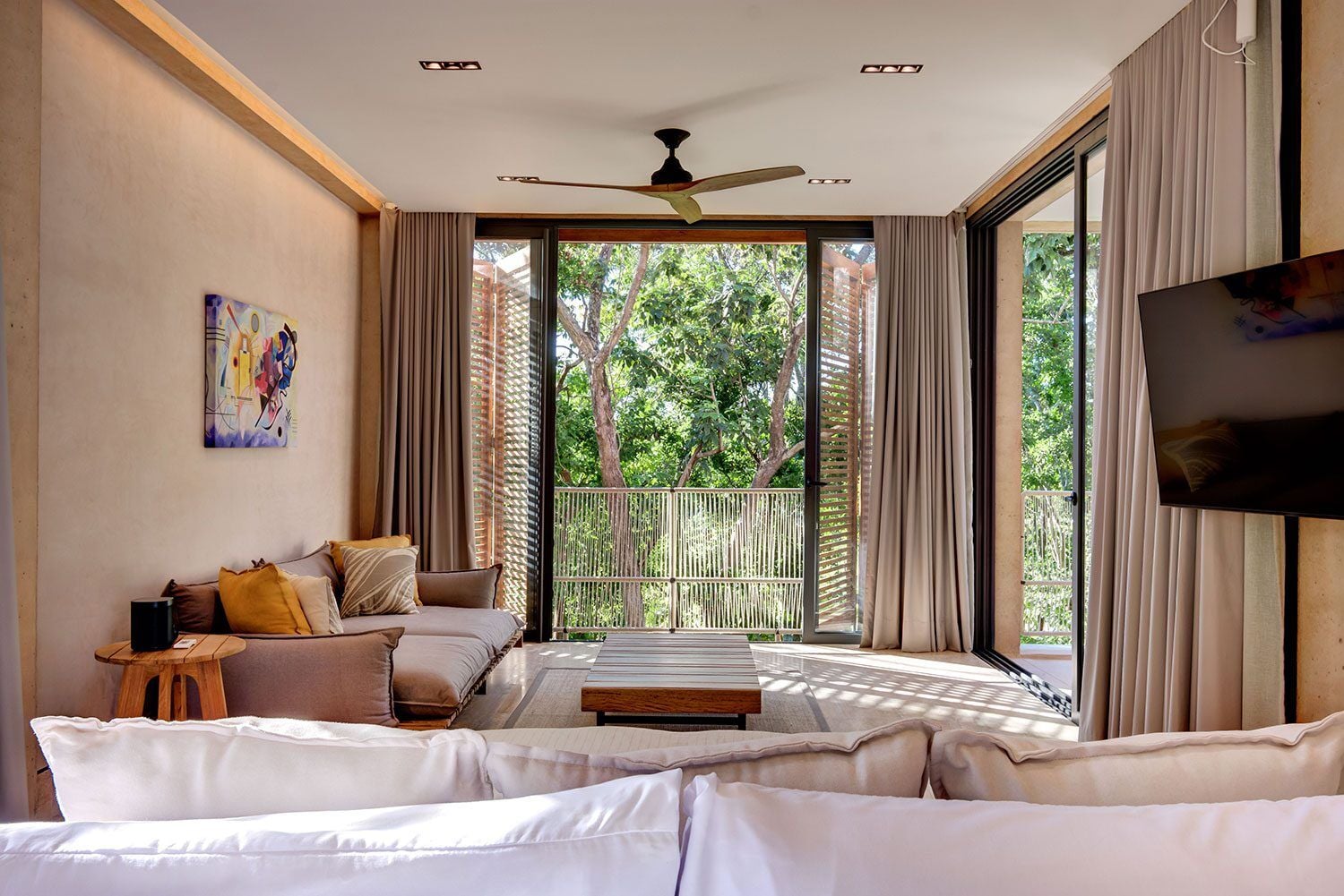 Palm Villa Experience lounge with a wall-mounted TV and tall garden windows — Playa del Carmen, Mexico