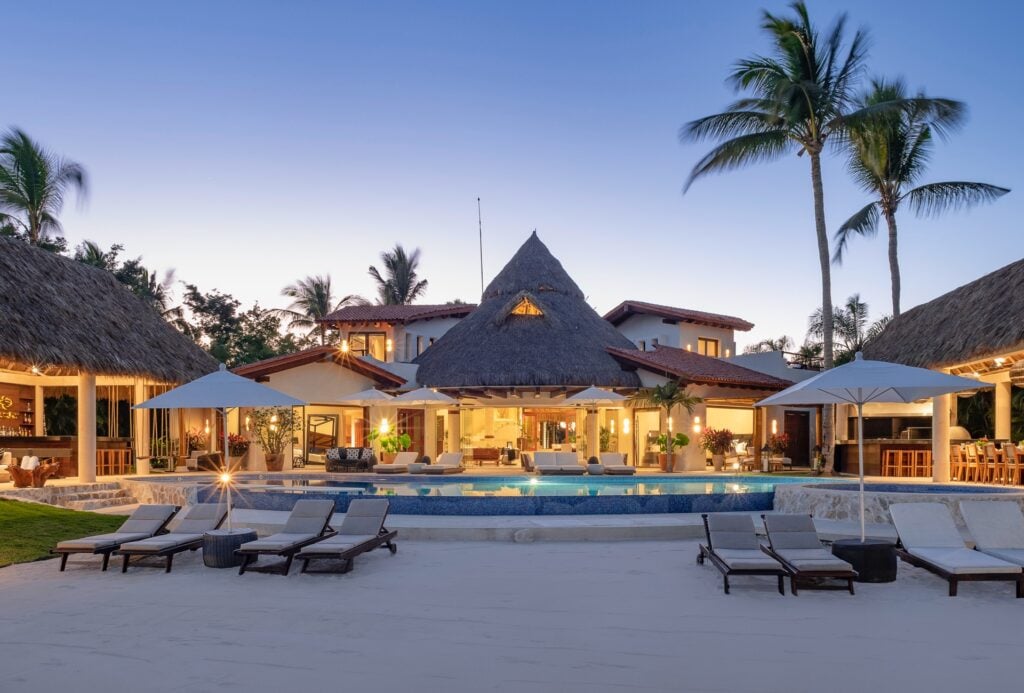 Casa del Faro exterior at dusk with lit thatched roofs, a pool, and loungers — Punta Mita Nayarit, Mexico