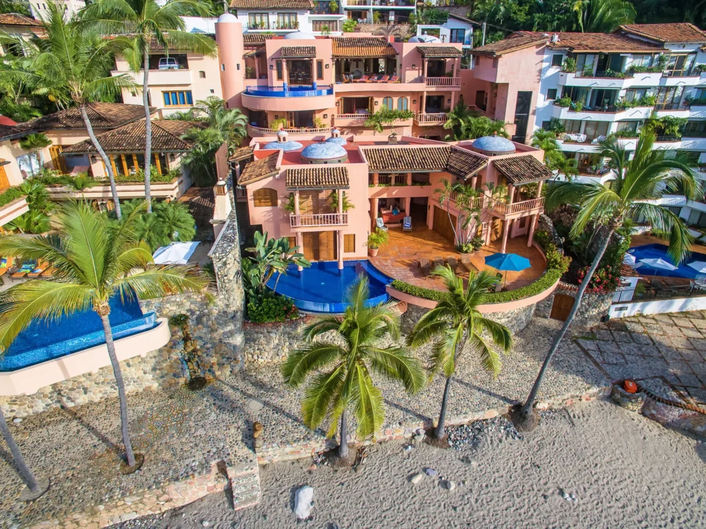 Villa Marea Alta aerial view of the pink villa and pools above a palm-lined shore — Puerto Vallarta, Mexico