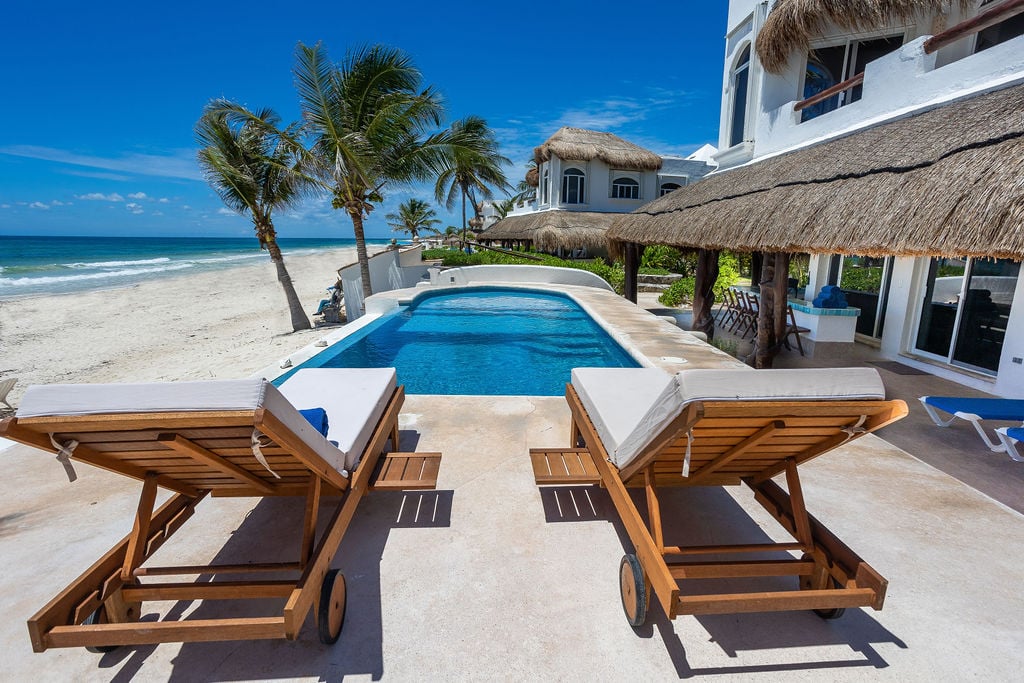 Villa Sarita two wood loungers facing the beachfront pool and palapa — Playa del Carmen, Mexico