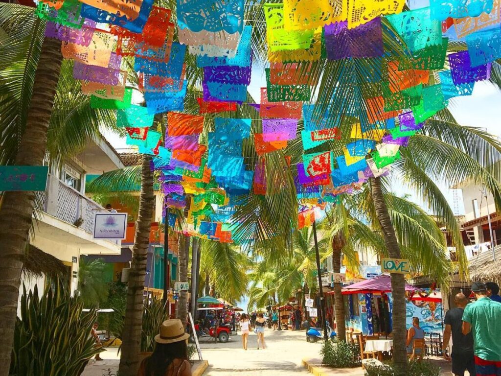 An image capturing the picturesque streets of Sayulita, Mexico, featuring colorful buildings, vibrant murals, charming shops, and lively street vendors.