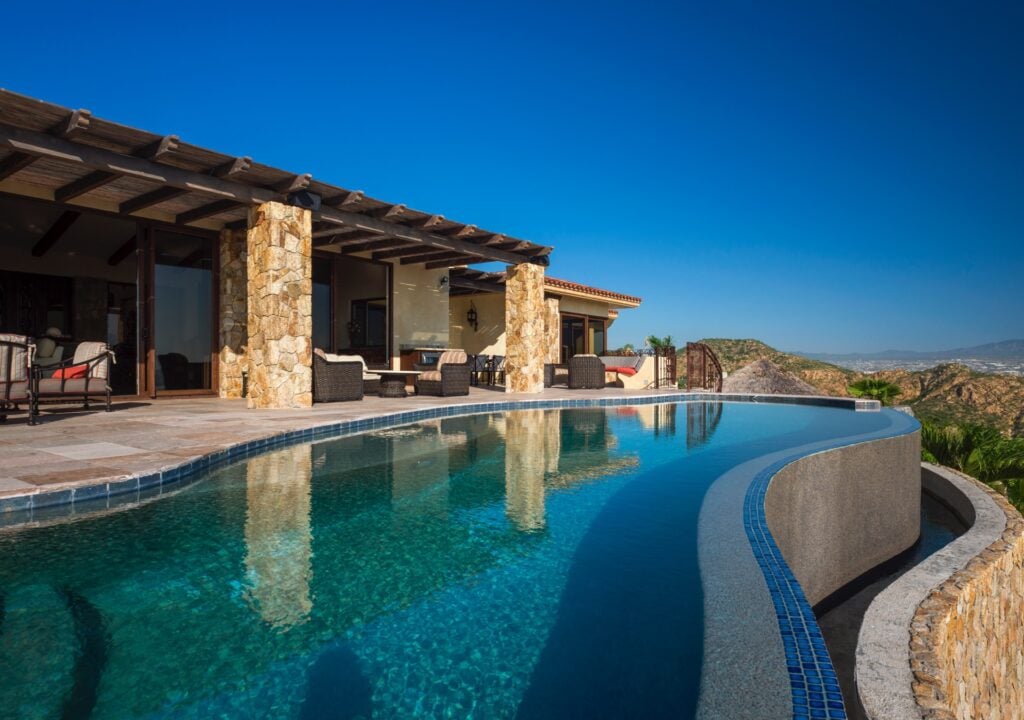 Casa Cielo blue-tiled infinity pool beside the covered patio and hills — Los Cabos, Mexico