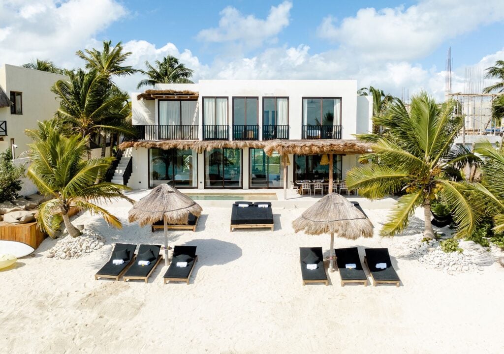Villa Zama beachfront exterior with loungers and thatched umbrellas on the sand — Tulum, Mexico