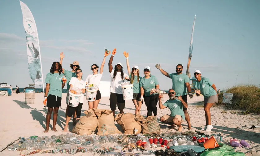 A group of volunteers participating in a beach cleanup in Tulum, Mexico, standing on the sand with bags of collected trash and recycling items, celebrating their efforts.
