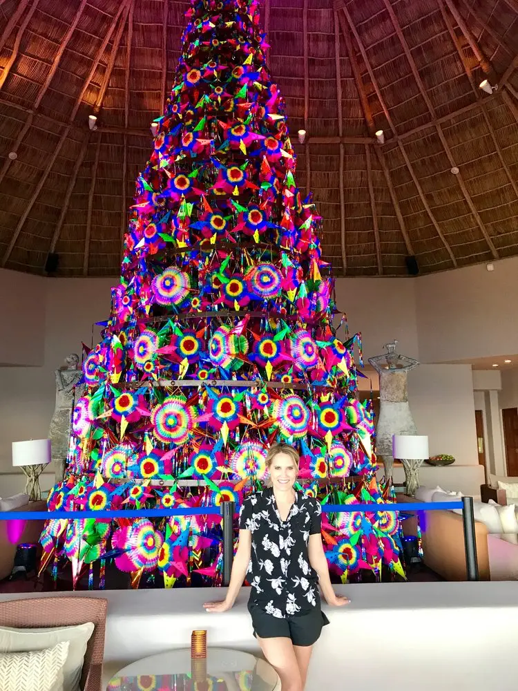 Individual in a floral shirt smiles before a colorful pyramid display in Punta Mita, Mexico's luxury Christmas villa.