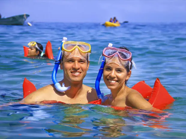 Couple snorkeling in clear waters, Punta Mita, Mexico; others kayak and snorkel under sunny skies—a Christmas getaway.