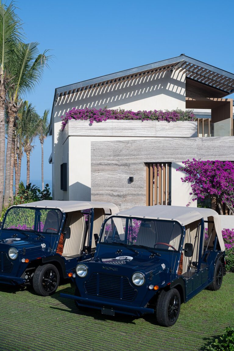 Two vintage golf carts parked near a modern Punta Pacifico building in Punta Mita, adorned with bougainvillea.