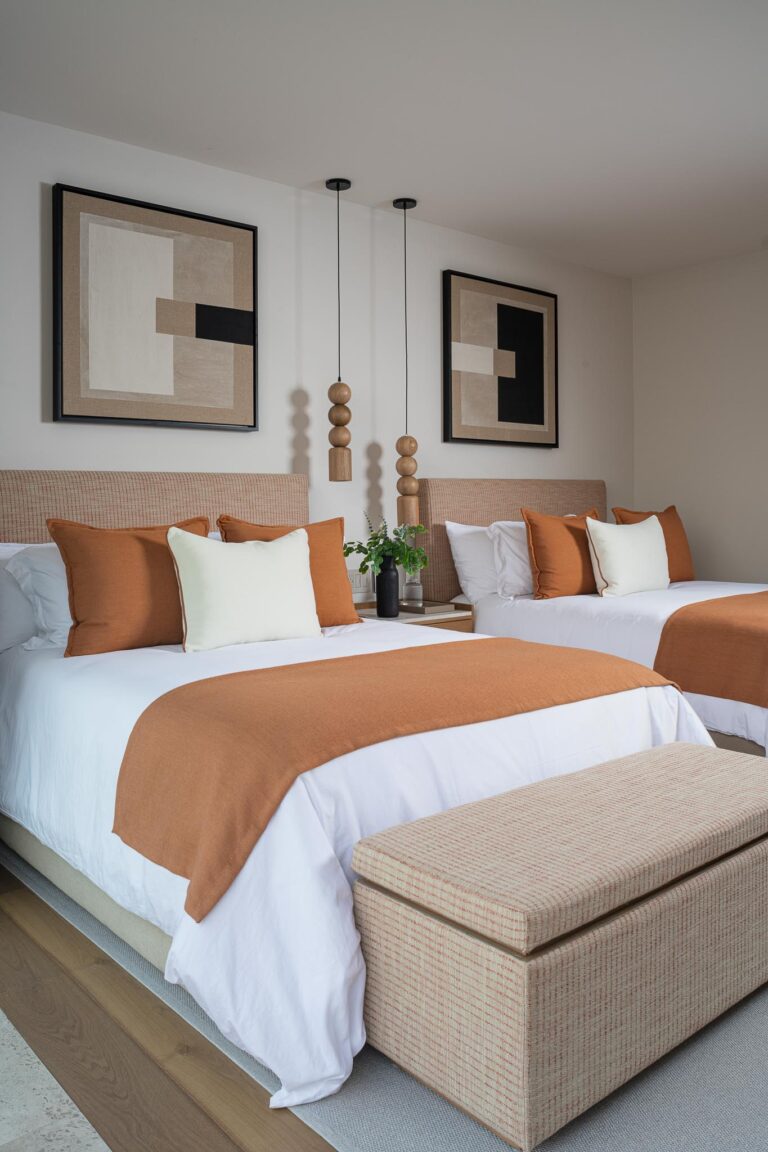 A modern Punta Pacifico bedroom features two beds with white-orange bedding, abstract wall art, and pendant lights.