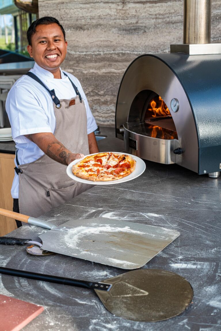 Chef at Punta Pacifico, Punta Mita, Mexico, presents pizza from a wood-fired oven in a traditional kitchen.
