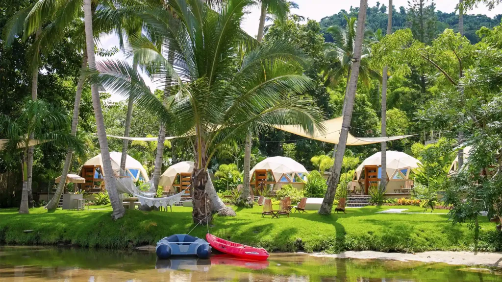 Geodesic domes at Santuario Yelapa Mexico Wellness & Yoga Retreat nestle by a pond amid palms, hammocks, and boats.