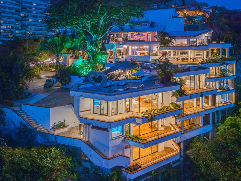 Hacienda Las Flores lit terraces stepping down the hillside below an uplit tree at dusk — Puerto Vallarta, Mexico