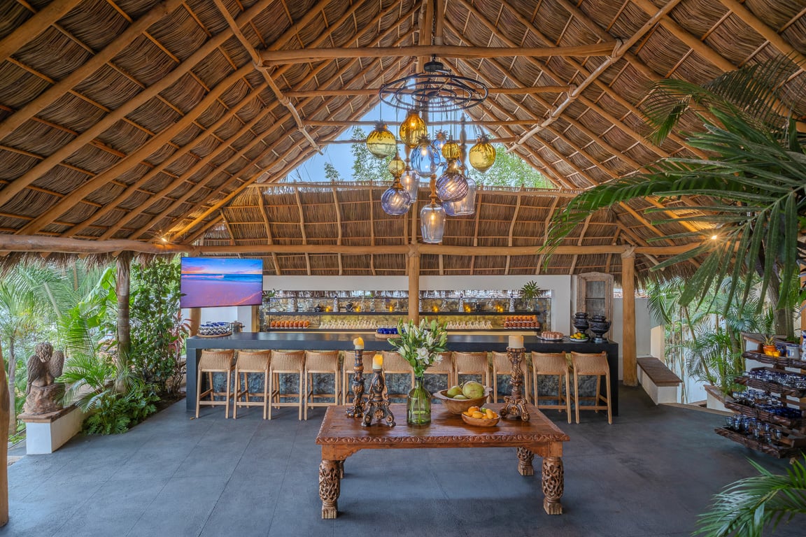 Hacienda Las Flores palapa bar with woven stools and a cluster of coloured glass lamps — Puerto Vallarta, Mexico