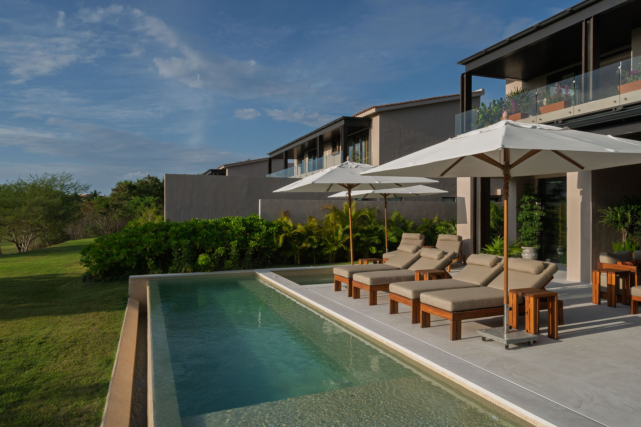 Villa Amada loungers under umbrellas along the pool at the lawn's edge — Punta Mita, Mexico
