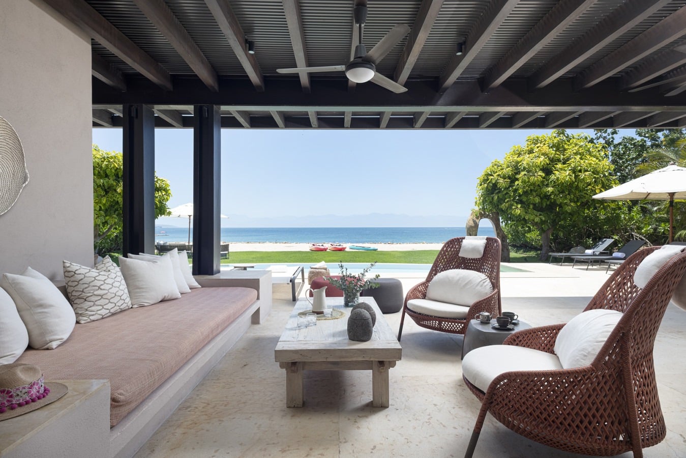 Villa Amistad shaded lounge with a built-in cushioned daybed and low stone table facing the sea — Punta Mita, Mexico
