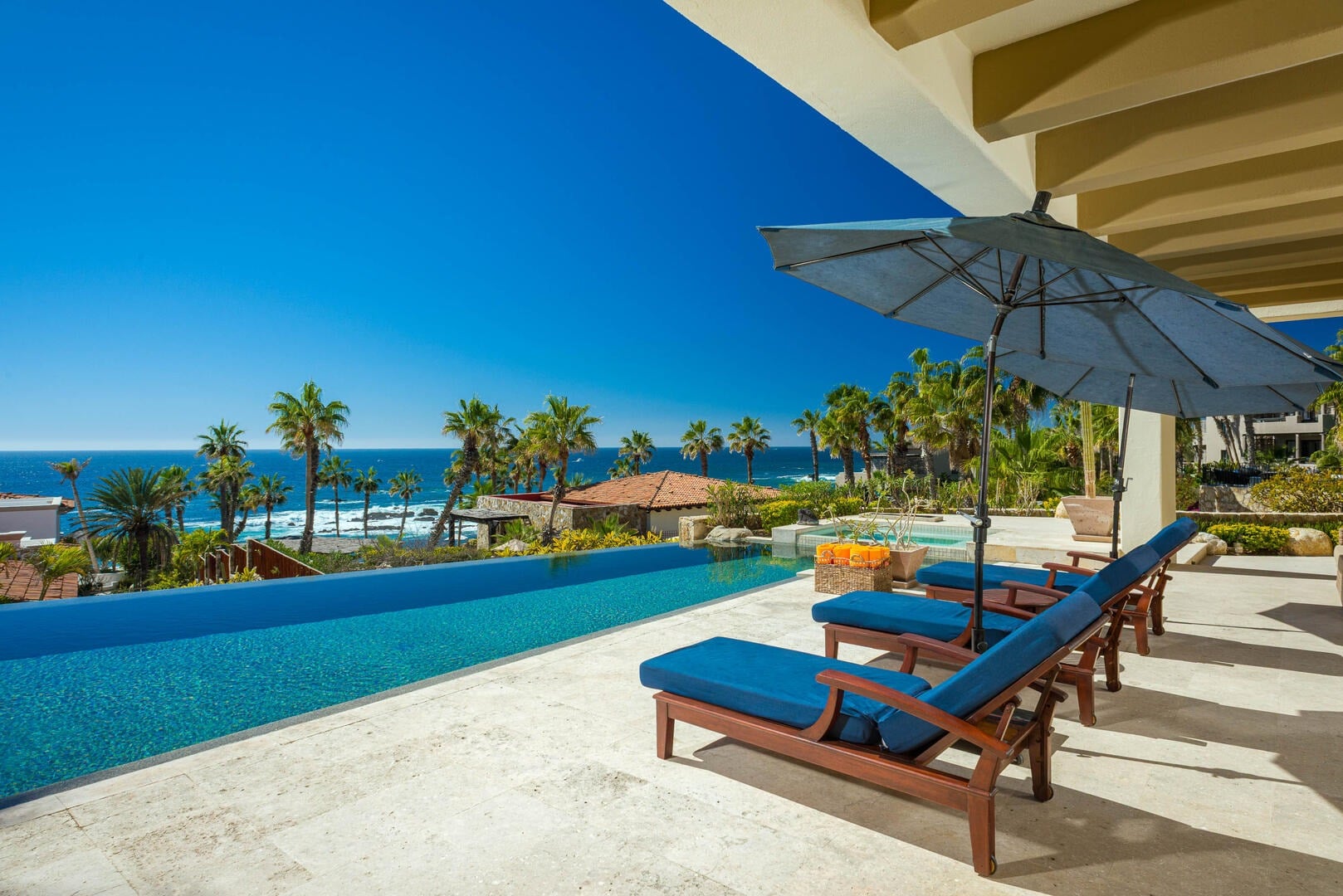 Villa Amistad blue-cushioned loungers and a blue umbrella beside the infinity pool above the sea — Punta Mita, Mexico