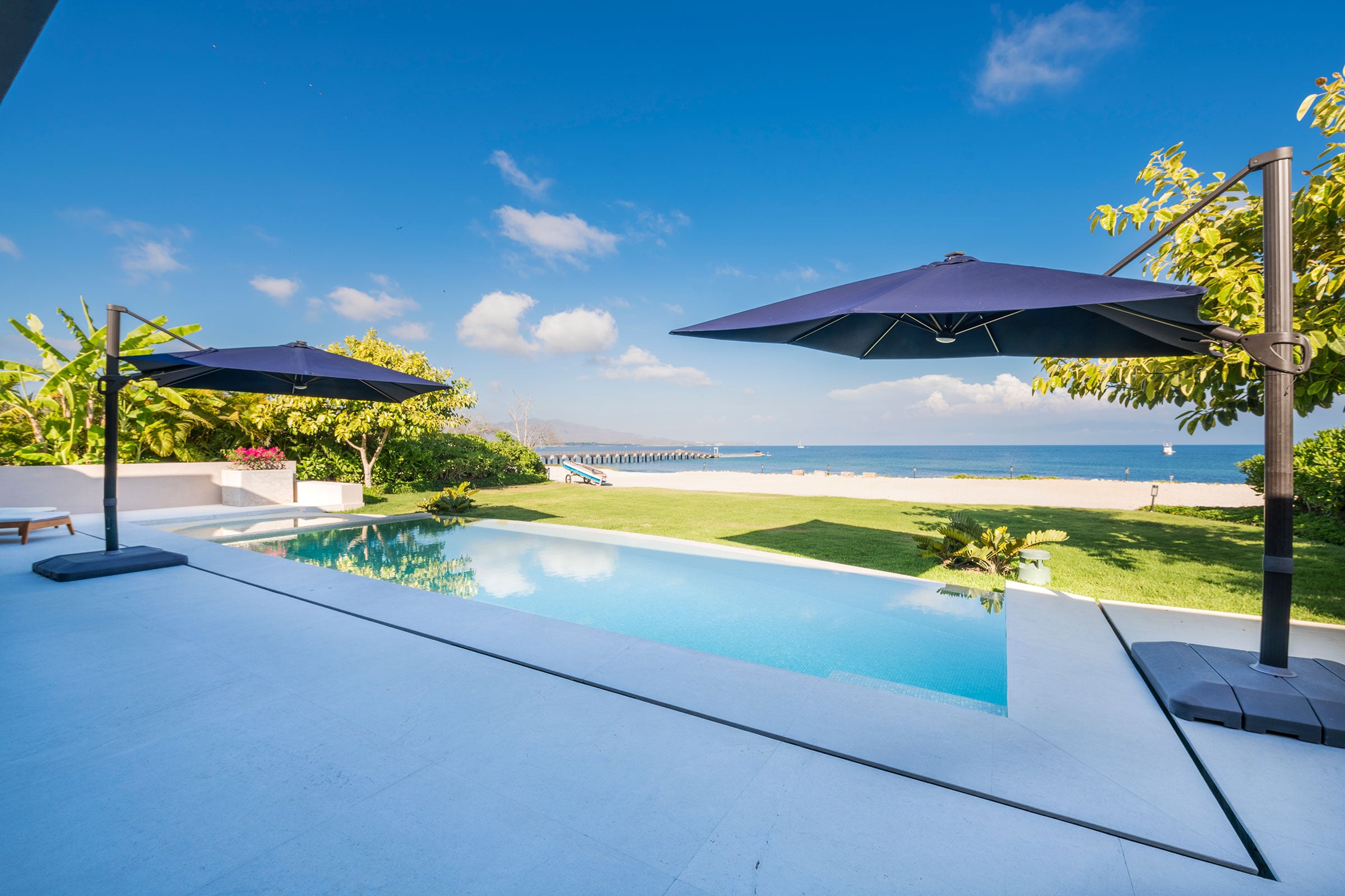 Villa Aurora infinity pool with umbrellas overlooking the ocean and pier — Punta Mita Nayarit, Mexico