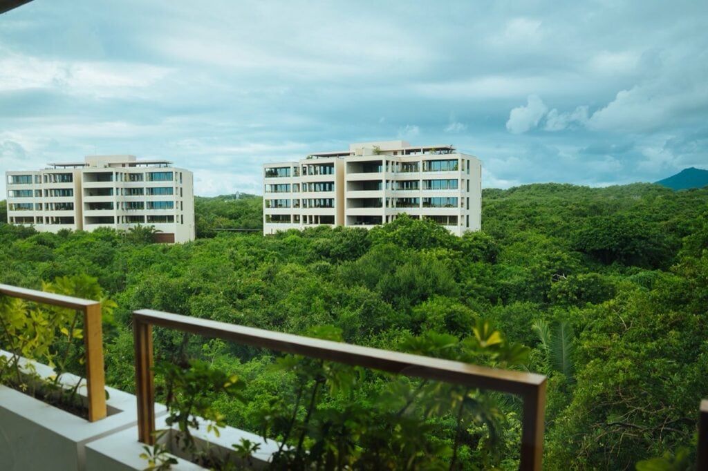 Condo Surf Residences 321 two white buildings beyond green treetops and a balcony railing — Punta Mita Nayarit, Mexico