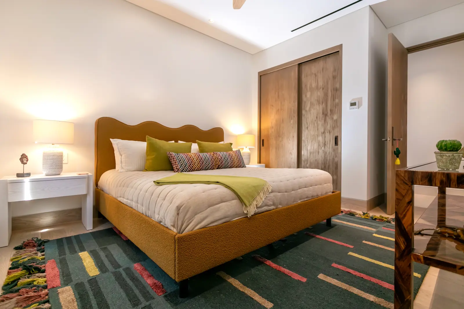 Bungalow 7 bedroom with a scalloped ochre headboard, green throw and striped rug — Los Cabos, Mexico