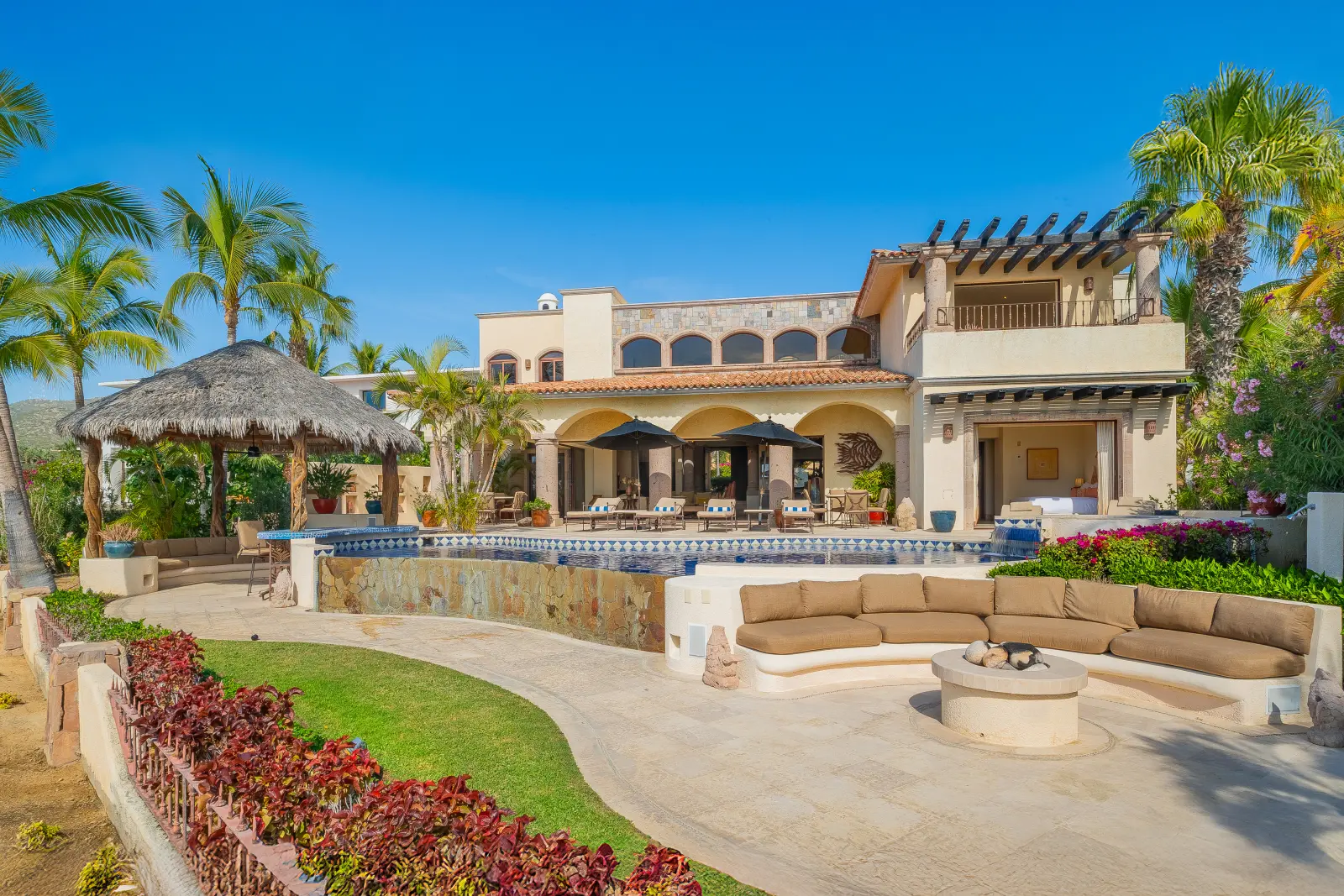 Casa Lolita the house behind its pool, palapa and curved sofa around a fire pit — Los Cabos, Mexico