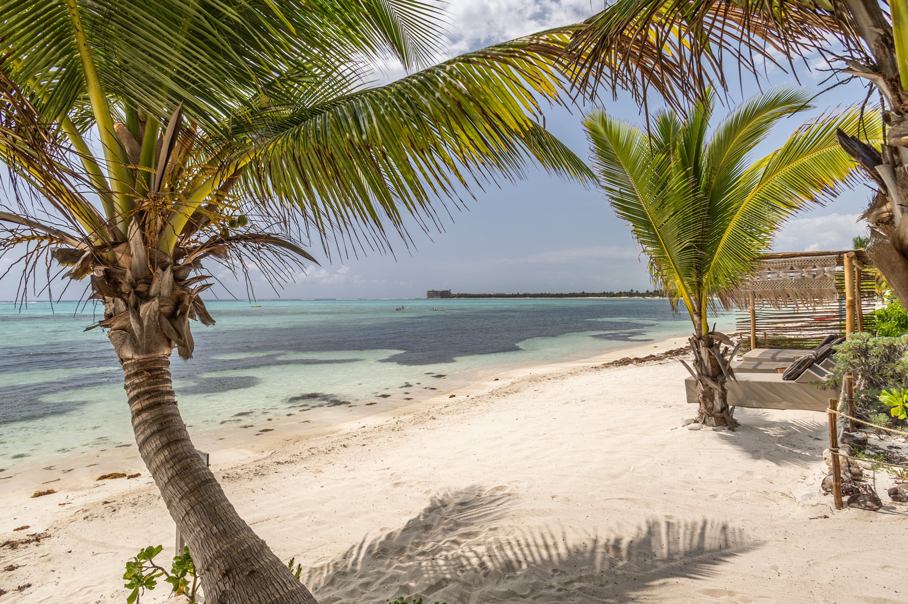 Casa Xixim white-sand beach with palms and a slatted shade structure — Tulum, Mexico