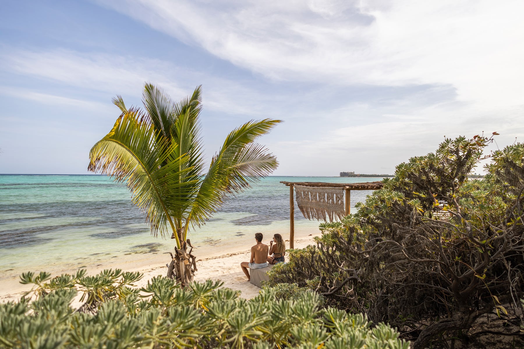 Casa Xixim two people seated beside a slatted beach shade facing the sea — Tulum, Mexico