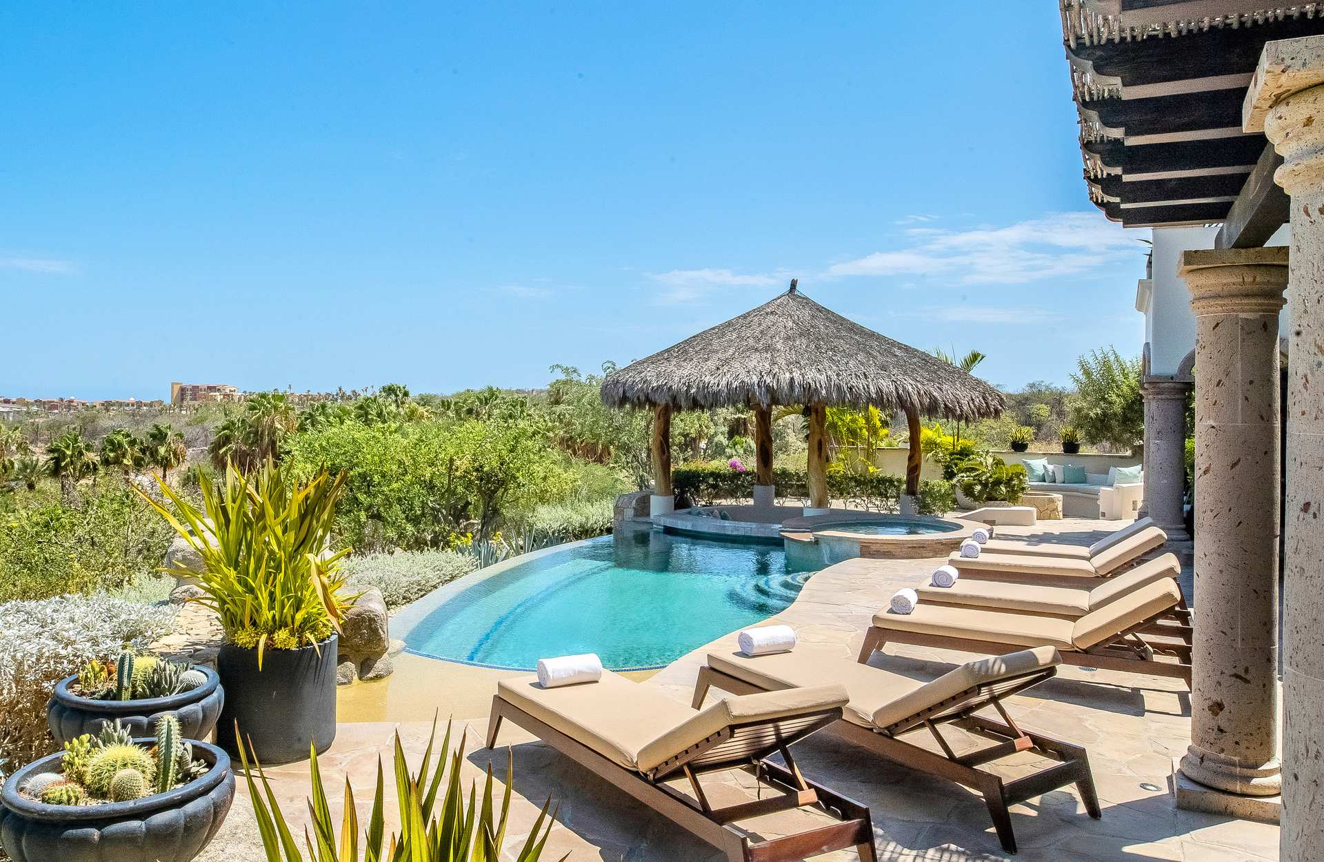 Villa Palmaritos 5 loungers with rolled towels beside the pool and thatched palapa — Los Cabos, Mexico