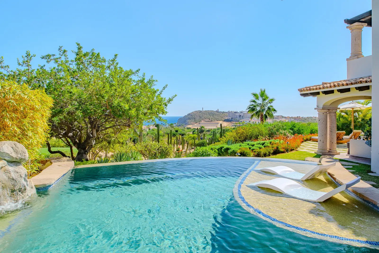 Villa Palmaritos 6 in-water loungers on the pool's tiled shelf below the trees — Los Cabos, Mexico