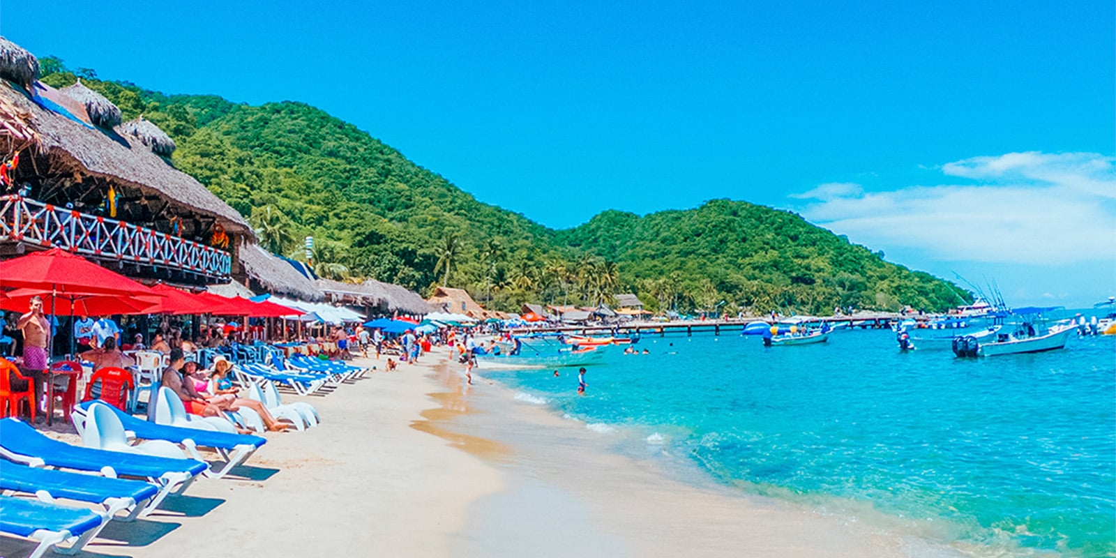 Playa Las Animas beach with palapa restaurants fishing boats on sand and swimmers in calm water Puerto Vallarta