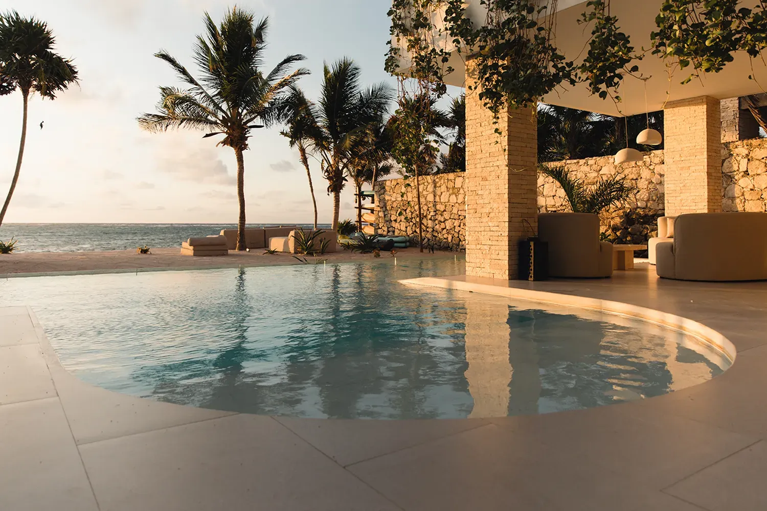 Studio 54 curved pool beside a stone-column lounge at sunset — Tulum, Mexico
