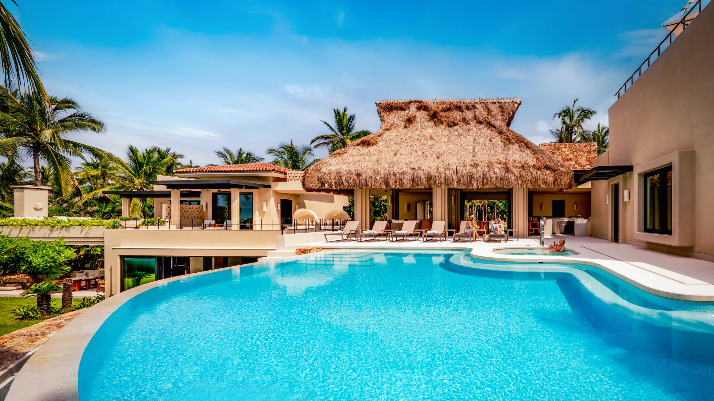 Casa Happy Paws curved swimming pool facing a thatched pavilion and palms — Punta Mita Nayarit, Mexico