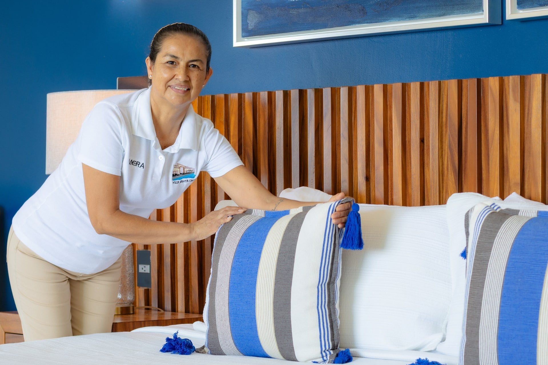 Villa Santa Cruz woman adjusting a striped pillow on a bed beside a blue wall — Puerto Vallarta, Mexico