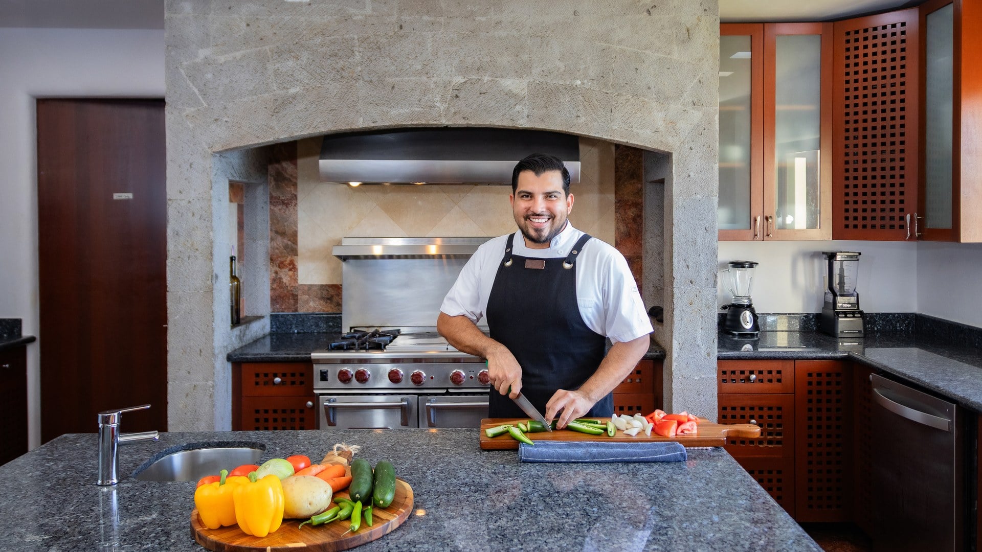 Villa Santa Cruz man slicing peppers at a kitchen island below a stone range hood — Puerto Vallarta, Mexico