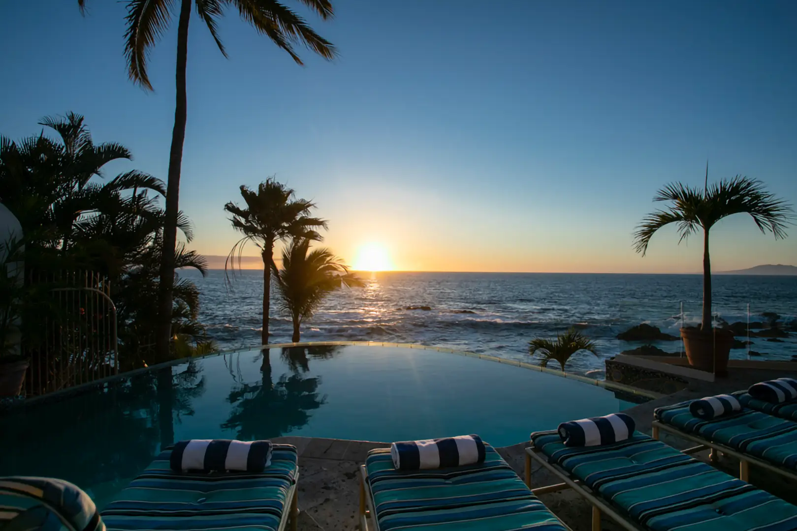 Casa Karma infinity pool and striped loungers facing the ocean at sunset — Puerto Vallarta, Mexico